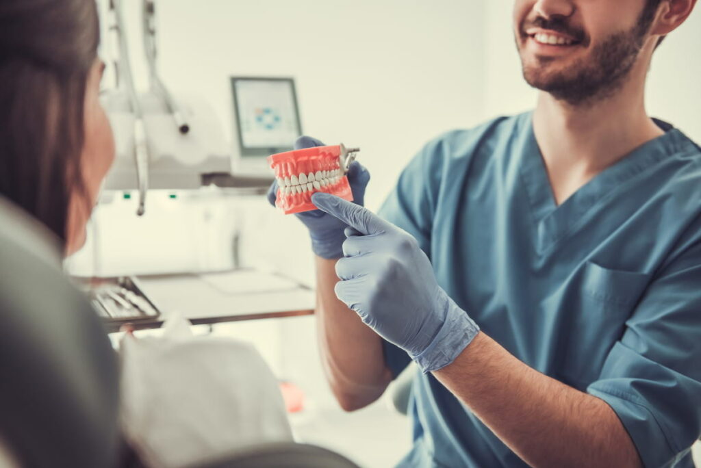 Handsome young dentist is showing his beautiful client dummy jaw and smiling