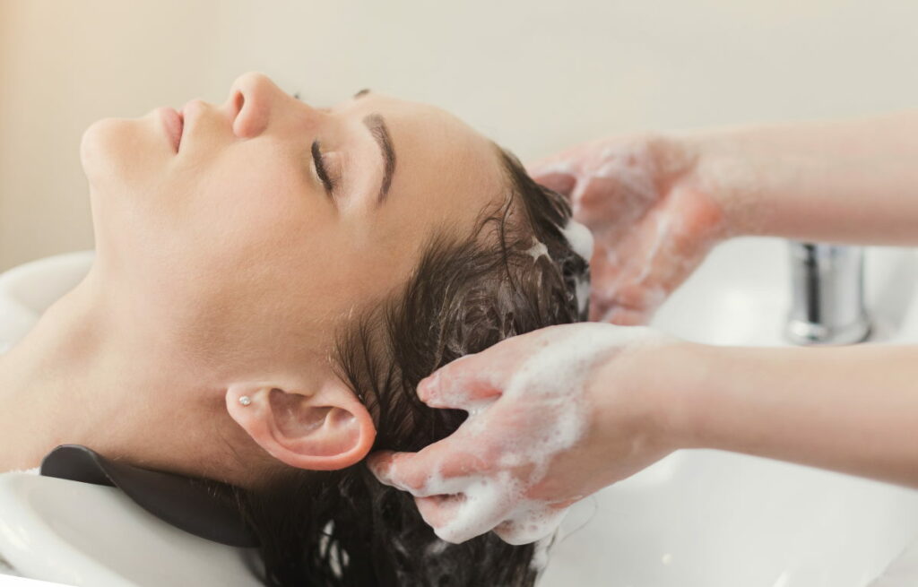 Happy young woman with hairdresser washing head at hair salon. Beauty and people concept