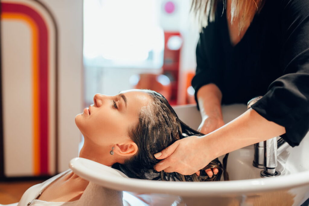 Hairdresser washes customer hair in basin, hairdressing salon. Professional haircutting in a beauty studio